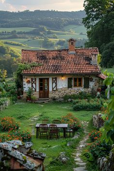 an old stone house sits in the middle of a lush green field with flowers around it