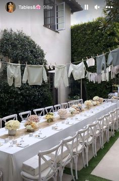 a long table is set up with white chairs and cloths hanging from the clothesline