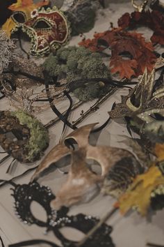 several masks are laying on a table covered with leaves and other decorations, including broccoli