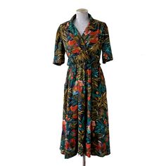 This cute vintage floral dress was sourced in London! The dress was likely made in the 80s and made to look a bit more retro. The bodice  and silhouette is reminiscent of the 40s. The tropical floral print is an interesting mix of rich aqua, burnt orange and teal, balanced with deep olives and yellow greens on a black background. The bodice of the dress has a double breasted collar, that is fastened with two black plastic buttons. The shoulder seams have a bit of a gather and sleeves are slightl Retro Printed Midi Dress, Vintage Short Sleeve Midi Dress For Vacation, Retro V-neck Midi Dress With Floral Print, Spring Retro Dresses With Tropical Print, Vintage Tropical Print Dresses For Spring, Vintage Dresses With Tropical Print For Spring, Retro Floral Print Midi Dress For Vacation, Vintage Floral Print Midi Dress With V-neck, Retro Collared Floral Print Dresses