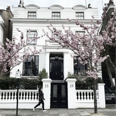 a woman walking down the sidewalk in front of a building with pink flowers on it