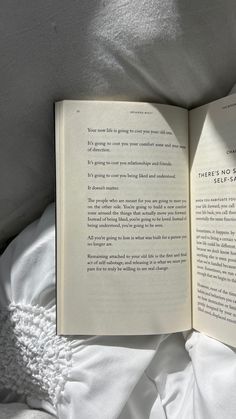 an open book sitting on top of a white bed next to a pillow and blanket