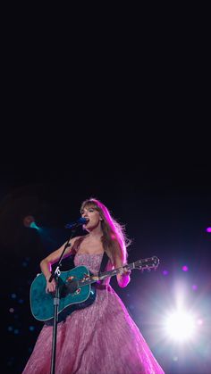 a woman in a pink dress holding a guitar and singing into a microphone on stage