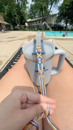 someone is tying a tie around a coffee cup on the edge of a swimming pool