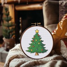 a cross - stitch christmas tree with lights on it in front of a fire place