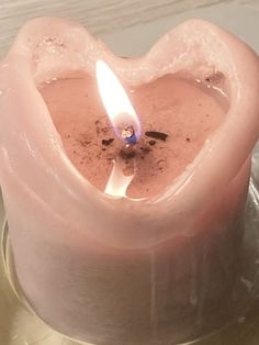 a pink heart shaped candle sitting on top of a metal plate with a lit candle in it