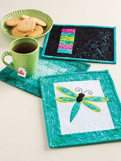 three placemats with dragonflies on them next to a cup of coffee and cookies