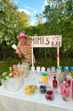 a woman in a pink hat standing behind a table with drinks and condiments