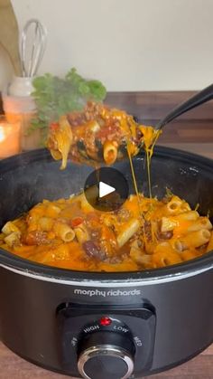 a slow cooker filled with pasta and meat being stirred by a ladle over it