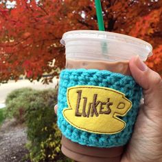 a hand holding a cup with a crocheted lid that says luke's