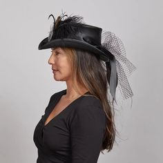 Fancy | Womens Victorian Leather Top Hat combines vintage charm with modern sophistication. Crafted from lightweight USA-made leather, this top hat is adorned with a satin black band and delicate mesh overlay, featuring a bow closure at the back and an antique medallion with feathers. Perfect for making a bold, elegant statement. Material: Lightweight USA Made Leather Shape: Top Hat Trim: Satin Black Band with Mesh Overlay, Bow Back Closure, and Antique Medallion with Feathers Brim Size: 2” Crow Black Leather Steampunk Top Hat, Elegant Black Leather Hat Band, Elegant Black Leather Hat, Top Hats For Women, Luis Guzman, Antique Medallion, Leather Top Hat, American Hat Makers, American Hat