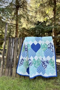 a blue and green quilt sitting on top of a wooden fence