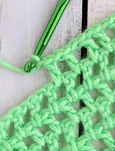 the crochet stitch is being worked on with a green knitting needle next to it