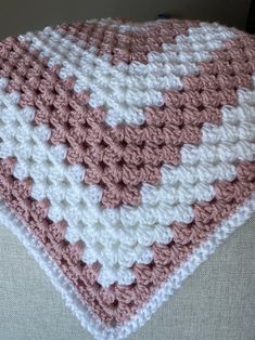 a pink and white crocheted blanket sitting on top of a couch