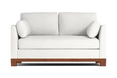 a white couch with two pillows on the armrests and a wooden frame in front of it