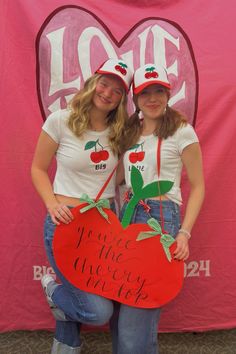 two girls in matching shirts holding up a heart shaped sign