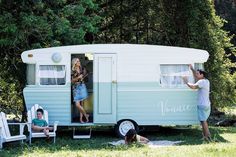 a man and woman standing in the doorway of an old camper trailer parked on grass