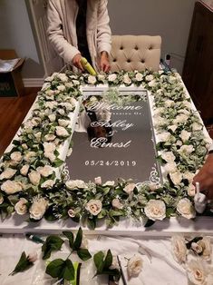 a woman cutting a cake with flowers and greenery on the table in front of her