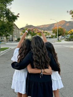 three girls standing in the middle of a street with their arms around each other's shoulders