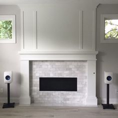 an empty living room with white brick fireplace and speakers in front of the fire place