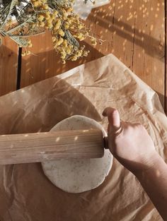 a person holding a rolling pin on top of a piece of paper next to flowers