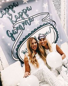 two beautiful women sitting on top of a bed next to each other holding white balloons