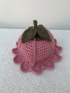 a pink knitted hat with a green leaf on the top sits on a white surface