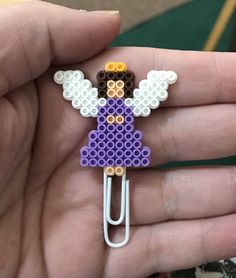 a person is holding a purple and white lego angel brooch with paper clip in their hand