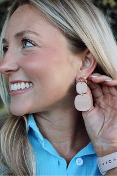 a woman smiles as she holds her ear up to the side while wearing a pair of earrings