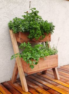 a wooden planter filled with green plants on top of a wooden floor next to a white wall