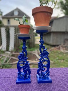 two blue candlesticks with plants in them sitting on a purple table cloth outside