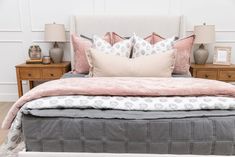 a bed with pink and grey pillows on it in a bedroom next to two nightstands