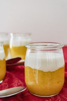 two jars filled with pudding sitting on top of a red table cloth next to spoons