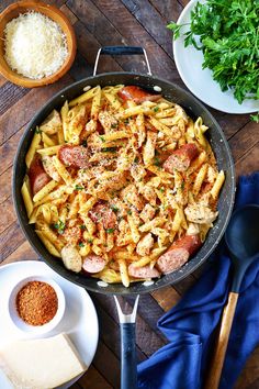 a skillet filled with pasta and meat on top of a wooden table next to other dishes