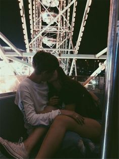 a man and woman sitting on top of each other in front of a ferris wheel