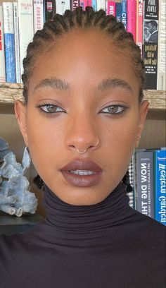 a woman with braids on her head standing in front of bookshelves and looking at the camera