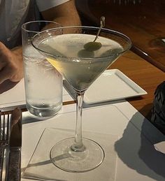 a man sitting at a table in front of a martini glass with an olive on it