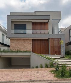 a modern house with wooden doors and brick steps leading up to the second floor balcony