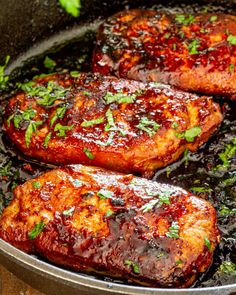 pork chops cooking in a skillet with sauce and parsley on the side