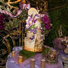 a fancy cake with purple flowers and butterflies on it sitting on top of a table