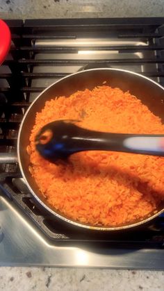 a frying pan filled with carrots on top of a gas stove next to a spatula