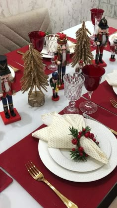 the table is set for christmas dinner with red place mats and gold cutleryware