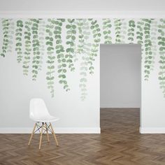 a white chair sitting in front of a wall with green leaves painted on the walls