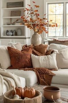 a living room filled with white furniture and lots of fall leaves on the coffee table