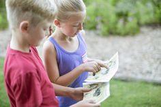 two young children looking at an open book in the grass, one boy is reading to the other