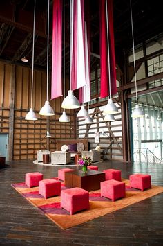 a living room filled with lots of pink furniture and hanging lights over the top of it