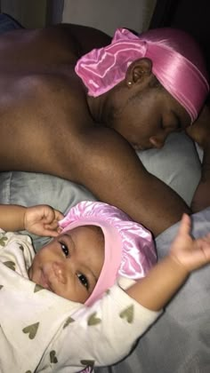 a man laying on top of a bed next to a baby in a pink hat