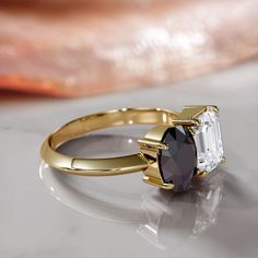 an engagement ring with two different colored stones on it, sitting on a white surface