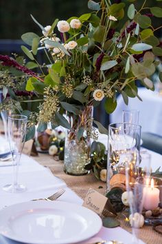 the table is set with candles, plates and vases filled with greenery on it