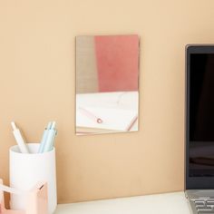 a laptop computer sitting on top of a white desk next to a cup and pen holder